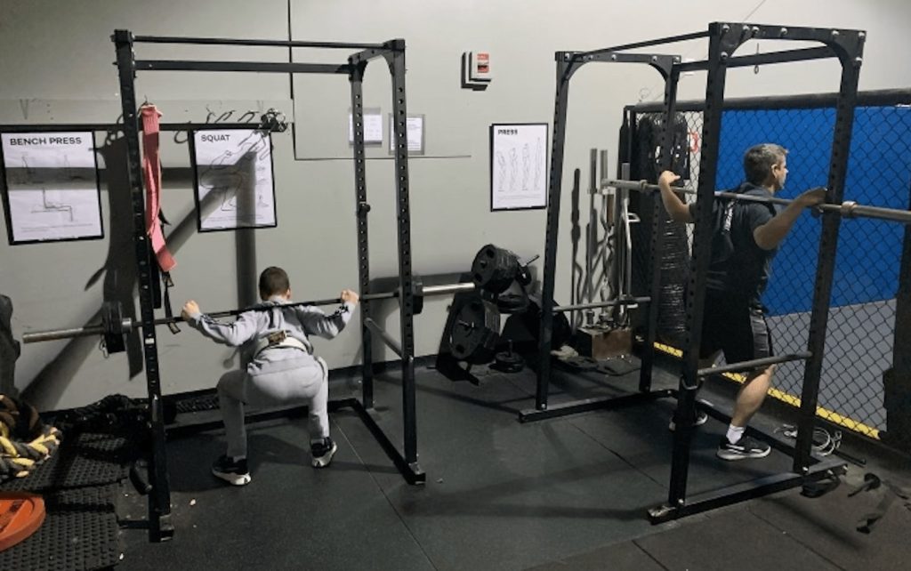 Two people practicing squats with the barbell